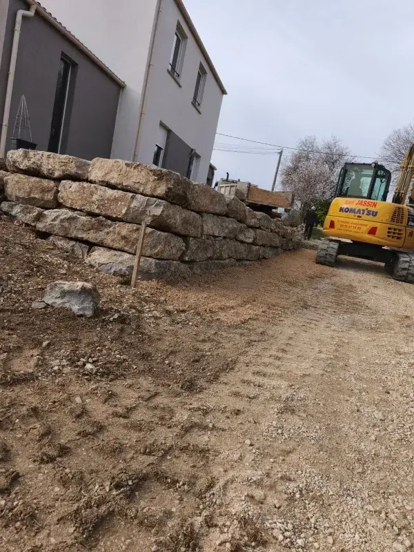 Création d’un mur de soutènement en pierres avec engin de chantier sur chemin d’accès